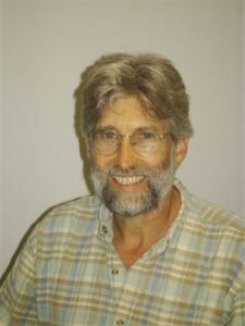 Image of an older man smiling. Head shot. Plain background.